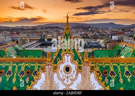 Budapest, Ungheria - vista aerea del famoso tetto colorato della tesoreria di Stato edificio con Bastione del Pescatore e golden sunset in background. Ro Foto Stock