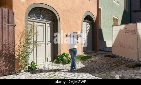 L'uomo porta grande formaggio gourmet ruota sulla sua spalla come egli rende la consegna a un negozio in una stretta strada di ciottoli nella città medievale di Rothenburg, Germania Foto Stock