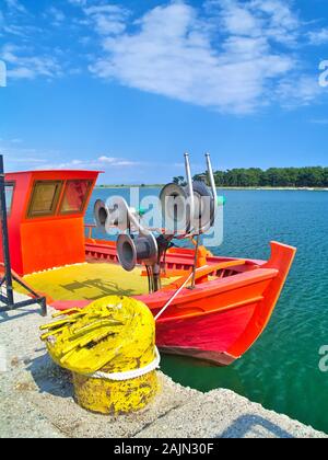 Porto Lagos, Grecia, dipinte di fresco vivido arancione barca e metallo giallo corde sotto il cielo blu con nuvole. Foto Stock