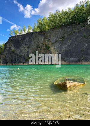 Barca abbandonata nella cava allagata con cristallo blu acqua. Sito subacqueo con freschi colori blu e acqua pulita per i subacquei poco abbandonato dissipatore in barca nel lago. Floreffe, Belgio. Foto Stock