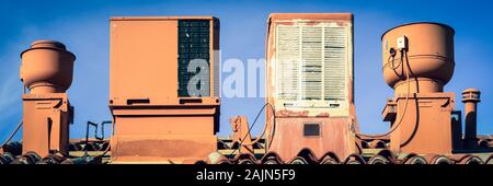 Un formato panoramico di un tetto con vecchio raffreddatore di palude, il condizionatore d'aria, aeratori e tubi di scarico tutte in un deserto piano colore contro un luminoso cielo blu Foto Stock