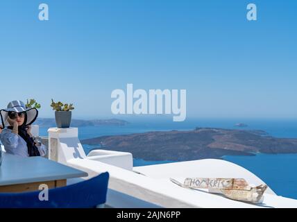 Fira, Santorini - 8 agosto 2019; Attracive donna siede rilassante in ombra sul balcone sull'isola greca Foto Stock