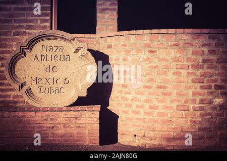 Off centrato vista di un tradizionale canto pietra intagliata per firmare il Plaza Antigua de Mexico in luce cruda contro un vecchio adobe un muro di mattoni in Tubac, AZ Foto Stock