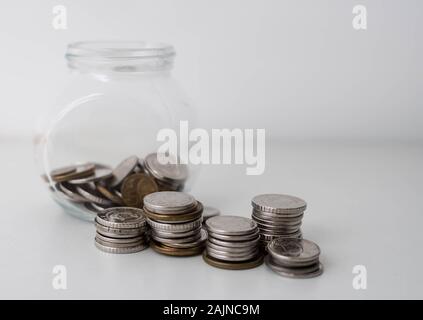 Pila di monete in una bottiglia di vetro su sfondo bianco. Di risparmio e di investimento Concetto del piano. Jar, monete, risparmio, investimenti, donazione. Le monete in un vaso Foto Stock