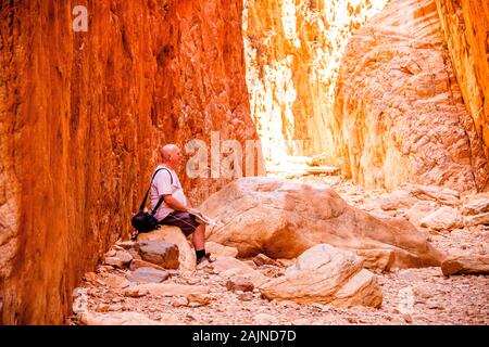 Un turista maschio si siede per ammirare Standley Chasm nel West MacDonnell Ranges in remoto del Territorio Settentrionale dell'Australia centrale. Foto Stock