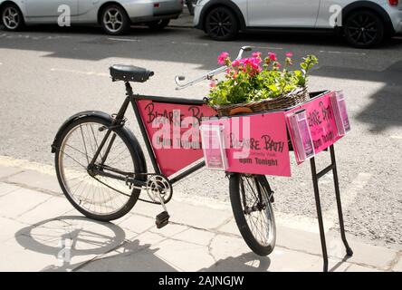 La bici del macellaio piantata con i fiori nella pubblicità del cesto in Camminata della commedia Foto Stock