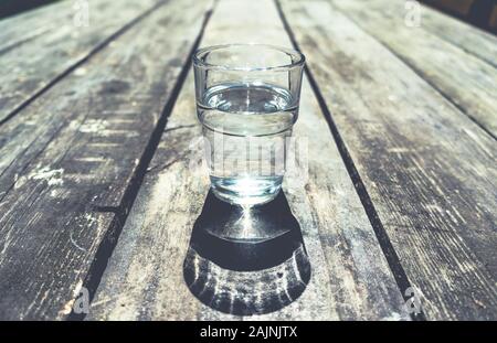 Close-up di un bicchiere di acqua chiara in piedi in mezzo di rozza tavola di legno Foto Stock