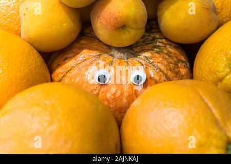 Concetto di zucca con gli occhi artificiali circondato da aranci, imitando per essere uno di loro. Foto Stock