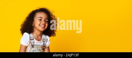 Carino piccolo nero ragazza ritratto, grazioso piccolo bambino ridere sinceramente, sorridente su sfondo giallo, lungo banner orizzontale, ampia shot, panorama Foto Stock