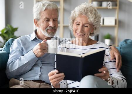 65s i coniugi in appoggio a casa Leggere libro bevanda potabile Foto Stock