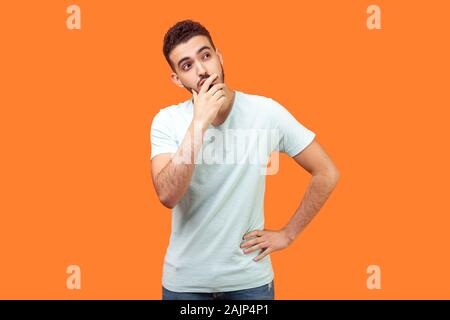 La necessità di pensare. Ritratto di pensosa brunette uomo con la barba bianca t-shirt tenendo la sua mento e scrutando idea, confuso non è sicuro di come soluzione. Foto Stock