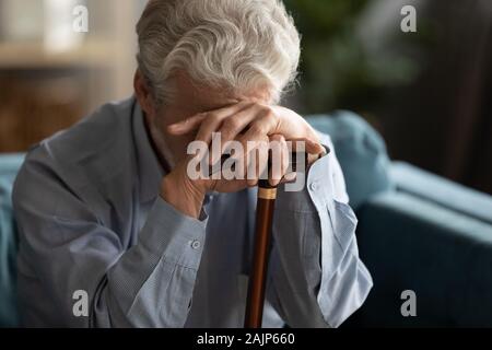 Triste uomo anziano che copre il volto con la mano che tiene la canna da zucchero Foto Stock