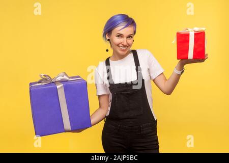 Ritratto di entusiasti felice di moda ragazza con violetta di capelli corti in tuta in jeans azienda presenta due grandi e piccole scatole, godendo del regalo di festa. Foto Stock