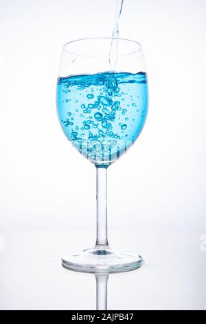 Cocktail blu è versata in un bicchiere su sfondo bianco con la riflessione, spruzzi e bolle Foto Stock