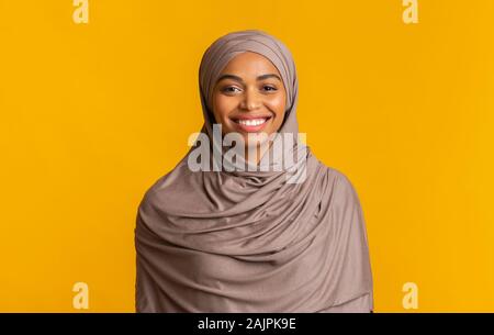 Ritratto di modesto musulmano nero ragazza di hijab sorridente alla fotocamera, posa su sfondo giallo, spazio vuoto Foto Stock