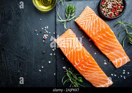 Materie filetto di salmone e gli ingredienti per cucinare, spezie e erbe su uno sfondo scuro . Vista superiore Foto Stock