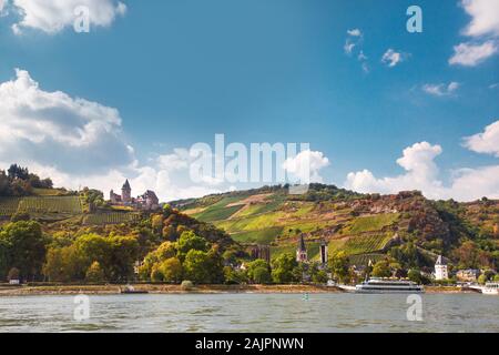 Splendido paesaggio panoramico tedesco di villaggio e vigneto a livelli lungo il fiume Reno con nave da crociera sul fiume in vista. Foto Stock