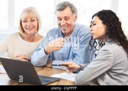 Bella ispanica agente di viaggio di lavoro con i clienti in ufficio, offrendo visite guidate a felice coppia di anziani Foto Stock