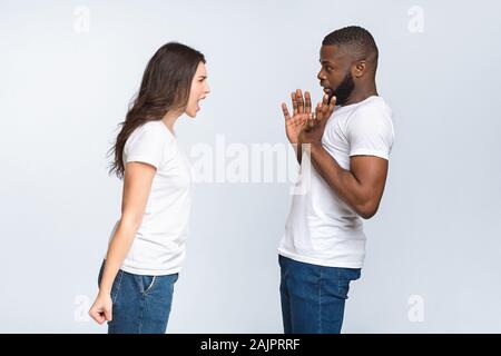 Giovane sostenendo. Arrabbiato giovane donna rimproverando a suo marito nero, emotivamente gridando, spaventata uomo alzando le mani cercando di proteggere se stesso, lo spazio libero Foto Stock