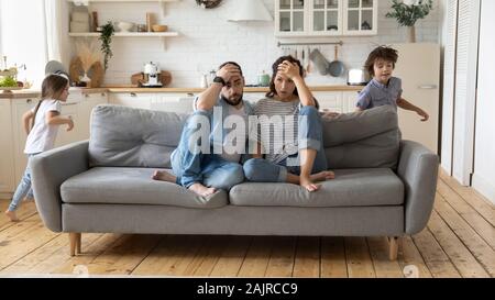 I genitori stanchi di rumorosi bambini che sono in esecuzione e urlando Foto Stock