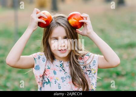 Poco sorridente ragazza raccolta di mele da albero in un frutteto Foto Stock