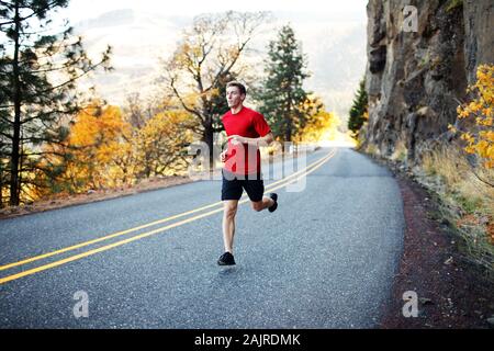 Runner maschile nella sua metà degli anni 20 che corre lungo la strada panoramica a Rowena Foto Stock