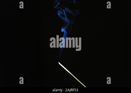 Incenso bastone sopra e togliere il fumo blu su uno sfondo blu. Foto Stock