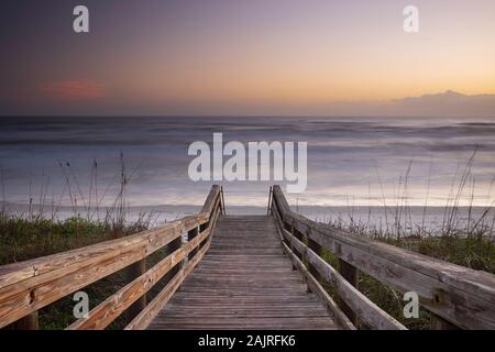 Un legno ponte pedonale, costruito su una duna di sabbia che è utilizzato per dare accesso alla spiaggia di Daytona Beach, Florida, si illumina durante una mattina sunrise. Foto Stock