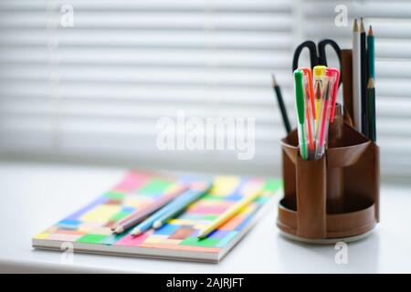 Articoli di cancelleria forbici e di una serie di matite colorate in una gabbia su un tavolo bianco. Foto Stock