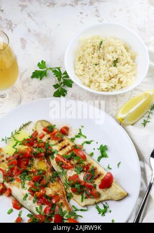 Branzino alla griglia servito su un piatto con pomodori freschi e decorato con prezzemolo e limone. Vista dall'alto Foto Stock