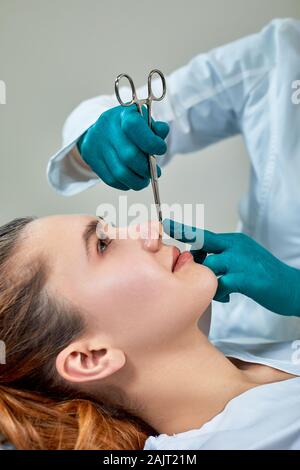 Lady con gesso sul naso, medico esaminare pazienti viso dopo un intervento di chirurgia plastica. Foto Stock
