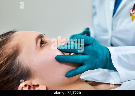 Lady con gesso sul naso, medico esaminare pazienti viso dopo un intervento di chirurgia plastica. Foto Stock