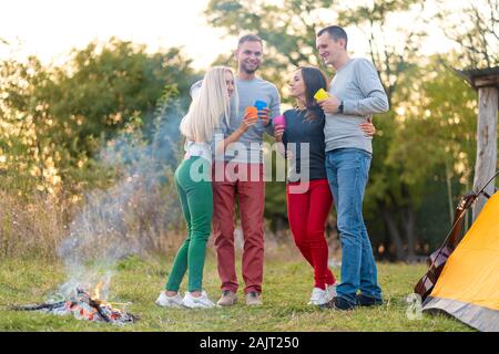 Picnic con gli amici mediante il fuoco. Amici di società aventi una escursione picnic sullo sfondo della natura. Gli amici raccontano storie. Picnic estivo. Buon divertimento con gli amici. Foto Stock