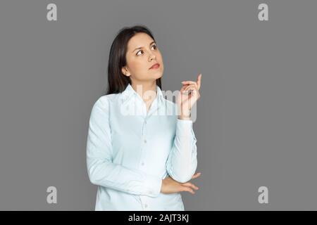 Alla ricerca di soluzione. Giovane donna in piedi isolato su grigio rivolto da parte riflessivo Foto Stock