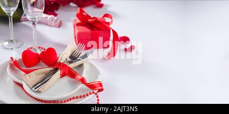 Il giorno di San Valentino sfondo. Forchetta e coltello nel cuore della piastra sulla tabella. Bottiglia di Champagne, bicchieri e confezione regalo su tavola Foto Stock