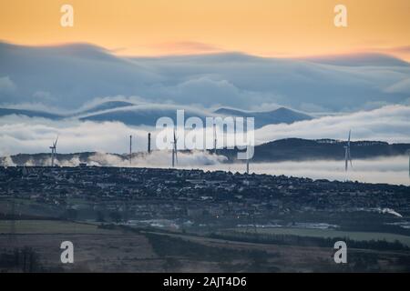 Fattoria eolica, impianto petrolchimico e la piccola città di Pentland Hills e nebbia di rotolamento in background. Foto Stock