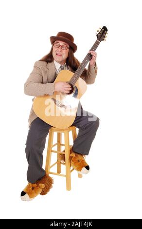 Un Medioevo uomo indigeni in scarpe di fantasia seduto e a suonare la chitarra in una camicia e hat, isolato per sfondo bianco Foto Stock