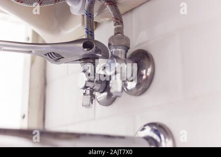 Plumber gira il dado su angolo valvola sotto il lavabo mediante diffusione di chiave. Foto Stock