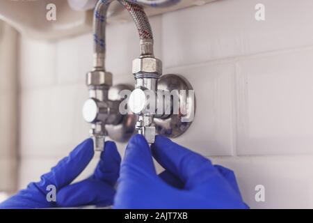 Plumber angolo di chiusura delle valvole di adduzione acqua calda e fredda sotto il lavandino per tubi flessibili di manutenzione o sostituire il rubinetto. Foto Stock