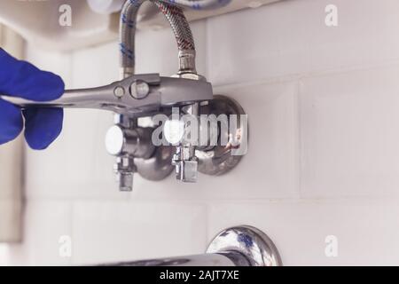 Plumber gira il dado su angolo valvola sotto il lavabo mediante diffusione di chiave. Foto Stock