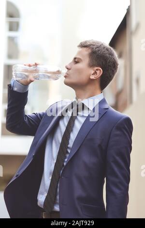 Uomo d affari con suit tenendo la bottiglia di acqua potabile e all'aperto. Il giovane uomo d affari bere acqua fresca Foto Stock