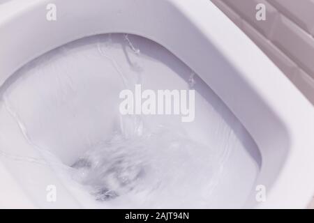 Vista ingrandita di un bianco di lavaggio wc. L'acqua volute nella tazza di gabinetto. Foto Stock