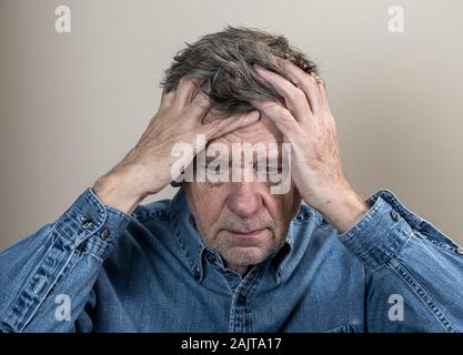 Testa e spalle ritratto di un anziano uomo caucasico con testa in mani e guardando premuto Foto Stock