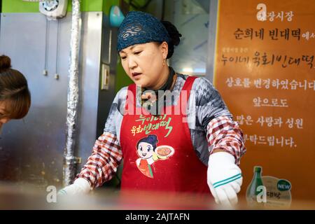 Chef coreano femminile cuoca bindaetteok (bindae-tteok, pancake di fagioli mung) su una griglia al mercato Gwangjang a Seoul, Corea del Sud. Foto Stock