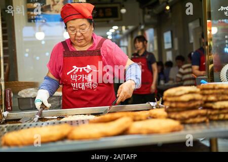 Chef coreano femminile cuoca bindaetteok (bindae-tteok, pancake di fagioli mung) su una griglia al mercato Gwangjang a Seoul, Corea del Sud. Foto Stock