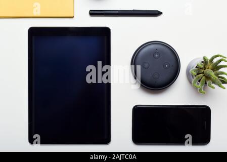 Digitale e la tecnologia wireless di oggetti disposti su una scrivania bianca tra cui telefono tablet e smart home altoparlante Foto Stock