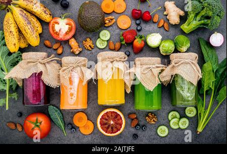 Colorati Frullati salutari e di succhi di frutta in bottiglie con fresca frutta tropicale e superfoods sulla pietra scura con sfondo spazio copia. Foto Stock