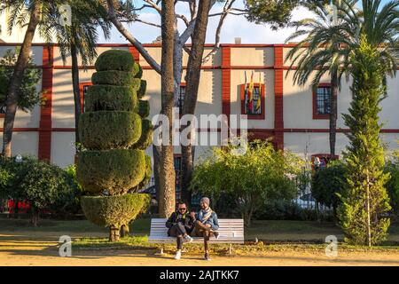 Due uomini siedono su una panchina del parco in un giardino paesaggistico, Cádiz, Spagna Foto Stock
