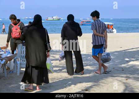 Donna musulmana tradizionale che indossa abiti neri con Harem pantaloni Gaucho e Hijab headwear alla spiaggia di Pattaya Thailandia Foto Stock
