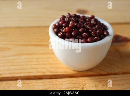 Una carta bianca comune e nuova ciotola di fagioli Adzuki, noto anche come red Mung bean, in close up, su una pianura tavolo in legno. Con copyspace. Foto Stock